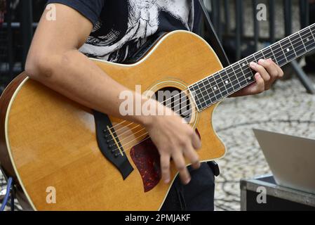 Man playing guitar at street event with black t-shirt. Arm and hands. Intentional background blur Stock Photo