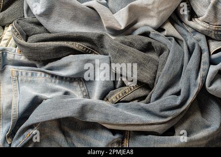 Lots of crumpled jeans pants, close up. Denim background. The concept of buying, selling, shopping and trendy modern clothes Stock Photo