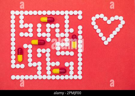 Being healthy is not easy. Sometimes it seems like the maze. Photo of a white and red-yellow pills maze on a red background. A heart made up of pills. Stock Photo