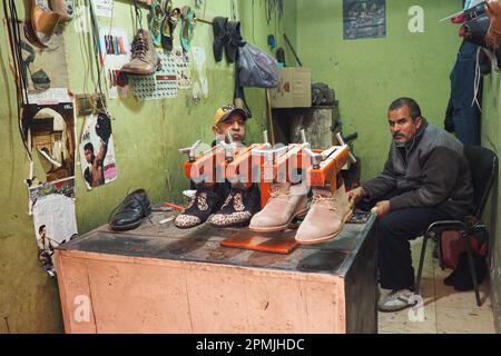 Marrakech, Morocco - January 1st, 2020: Two unknown men sitting in their shoes repair small workshop on street side Stock Photo