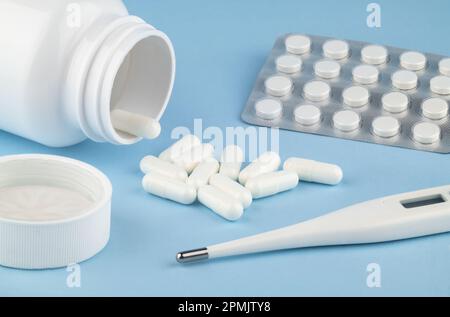 Drugs and health supplement pills poured from a medicine white bottle health care and medical and thermometer top view on colored blue background. Stock Photo