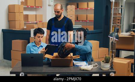 Business owners checking quality of supplies before packing them in carton boxes, putting merchandise for shipping. People working together on warehouse shipment, retail distribution. Stock Photo