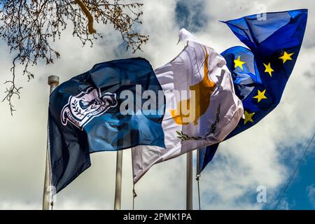 Three flags fly together against a cloudy sky in Pedoulas, Republic of Cyprus: a dark blue flag bearing a crest, the Cypriot flag and the flag of the European Union. Stock Photo