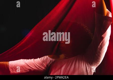 Portrait of a woman with red cloth stretched in front of her face. isolated on black background. Stock Photo