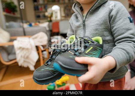 Frankfurt, Germany - Mar 12, 2023: A child showing modern, stylish Lowa boots with vibrant blue and green design. Waterproof and insulated for warmth in cold winter conditions. Stock Photo