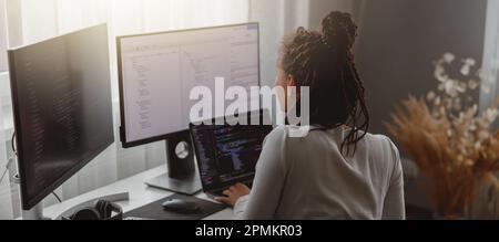 Rear of young woman looking at computer screen while working programming on laptop Stock Photo