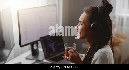 Side view of cheerful young female wearing headphones and programming on computer Stock Photo