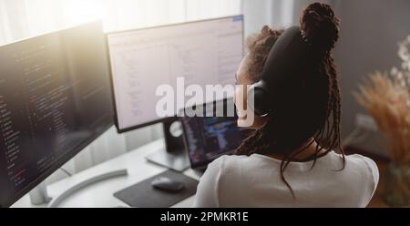 Back view of young professional woman programmer working from home sitting at desk Stock Photo