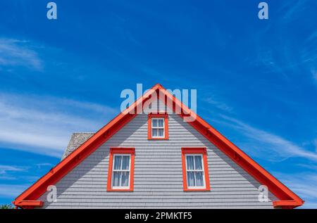 Side-gabled dwelling in gray shingle cladding. Orange is being used as an accent color on trims and roof edging, making them pop against the blue sky. Stock Photo