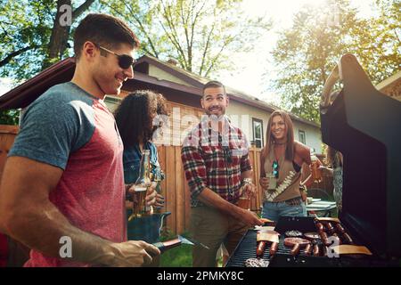 Having a chilled time with friends around the barbecue. a group of friends having a barbecue outside. Stock Photo