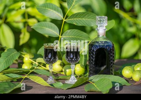 Liqueur from young green walnuts, remedy for stomach ache, close up. Tincture of green walnuts in a glass bottle on a table in the garden Stock Photo