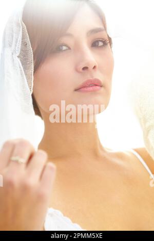 Veiled in romance. A beautiful young Asian bride wearing a lace veil. Stock Photo