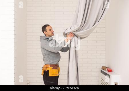 worker installing window curtain rod on the wall. Stock Photo