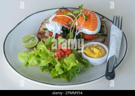 Toast with poached eggs, tomato and salmon on plate in cafe, close up, breakfast time Stock Photo