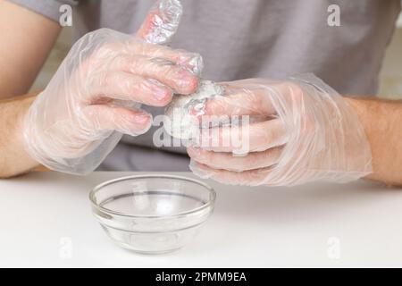 A man puts disposable plastic transparent gloves on his hands to dye Easter eggs. Coloring of Easter eggs. Stock Photo