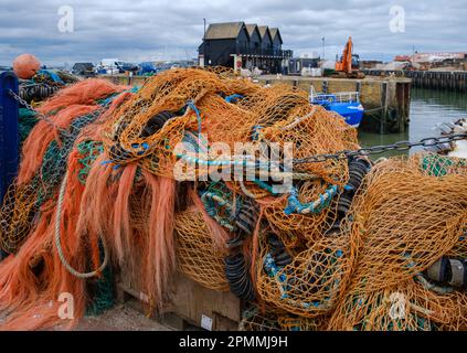 Close-up view of orange fishing nets with wooden huts and fishing boats in background at Whitstable Harbour North Kent coast, England, UK. Stock Photo