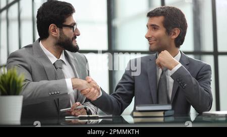 sitting at table wile advisor and investor shaking hands over table in office Stock Photo