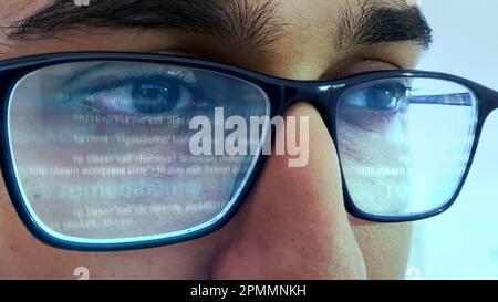 A man working on computer looking at programming code reflecting in his glasses Stock Photo