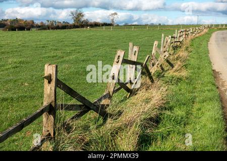 Old rotten, dilapidated, broken, tumbledown, wooden post and rail fence by farm field, England, UK Stock Photo