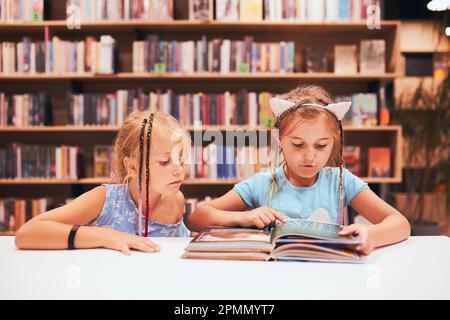 Two elementary schoolgirls doing homework in school library. Students learning from books. Pupils having fun in library. Back to school Stock Photo