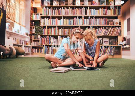 Two primary schoolgirls doing homework in school library. Students learning from books. Pupils having fun in library. Back to school Stock Photo