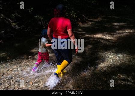 An Ecuadorian migrant, accompanying her daughter, walks through the river in the dangerous jungle of the Darién Gap between Colombia and Panamá. Stock Photo