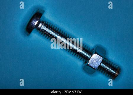 Standard hex nut and matching hex bolt arranged on a clean blue background in a minimalist studio composition. Stock Photo