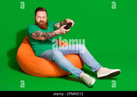 Full length photo of angry upset man wear t-shirt sitting bean bag losing playstation game empty space isolated green color background Stock Photo