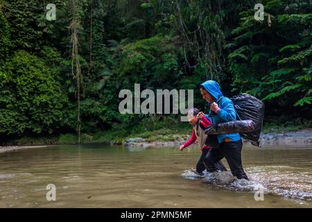 An Ecuadorian migrant, accompanying his daughter, walks through the river in the dangerous jungle of the Darién Gap between Colombia and Panamá. Stock Photo
