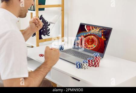 Excited young man is happy about his victory playing online casino at home on laptop. Stock Photo