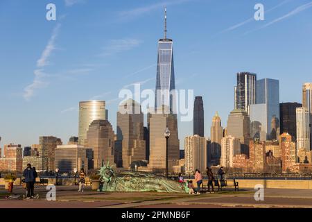 he sun sets on the 'Reclining Liberty' statue by artist Zaq Landsberg in Liberty State Park as it sits in front of the skyline of lower Manhattan and Stock Photo