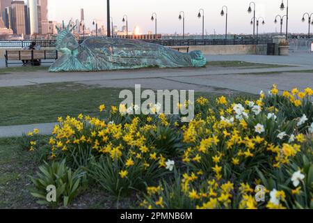 he sun sets on the 'Reclining Liberty' statue by artist Zaq Landsberg in Liberty State Park as it sits in front of the skyline of lower Manhattan and Stock Photo