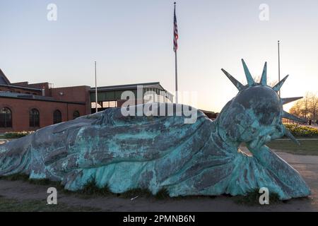 he sun sets on the 'Reclining Liberty' statue by artist Zaq Landsberg in Liberty State Park as it sits in front of the skyline of lower Manhattan and Stock Photo