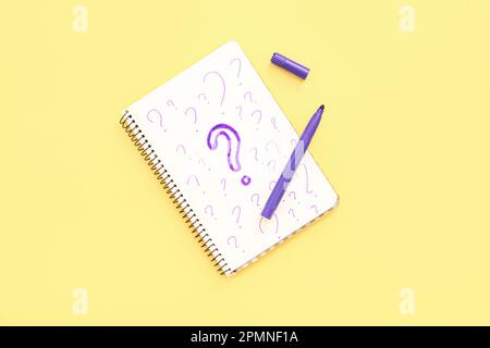 Notebook with drawn question marks and marker on yellow background Stock Photo