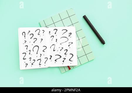 Notebooks with question marks and marker on green background Stock Photo