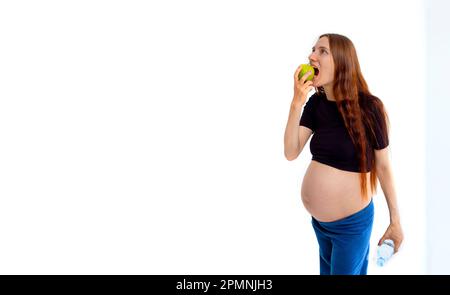 Pregnant woman propose apple for her belly copy space. Beautiful expectant lady having fresh snack, gray studio background. Healthy nutrition and Stock Photo