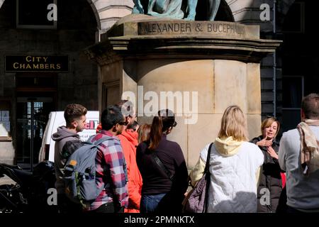 Edinburgh, Scotland, UK. 14th April 2023. Good weather encourages the Easter holidaymakers to frequent the usual visitor attractions and hotspots, with numerous tour parties and tour guides filling the streets. Tour guide at the City Chambers under the statue of Bucephalus. Credit: Craig Brown/Alamy Live News Stock Photo
