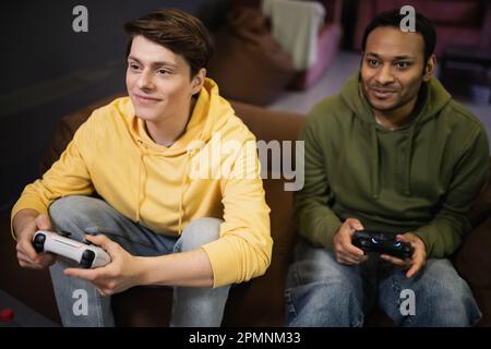 KYIV, UKRAINE - FEBRUARY 13, 2023: Pleased man playing video game with indian friend in gaming club,stock image Stock Photo