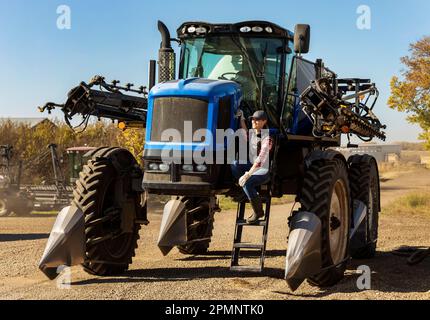 Portrait of a woman farmer sitting on the steps of a tractor with seeder attachments; Alcomdale, Alberta, Canada Stock Photo