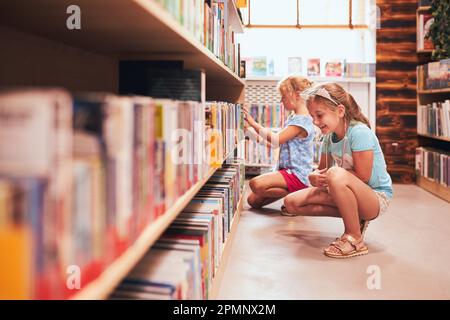 Two schoolgirls choosing books in school library. Primary school students learning from books. Children having fun in school club. Back to school. Doi Stock Photo