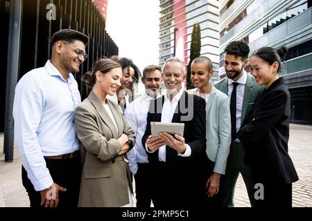 Group of successful multiracial corporate business team looking at tablet in the financial district. Smiling multiethnic professional employees Stock Photo