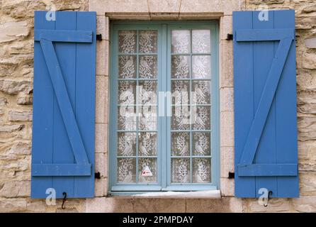 Lace curtain adorned with birds inside a window with blue shutters; Cap-Chat, Gaspe, Quebec, Canada Stock Photo