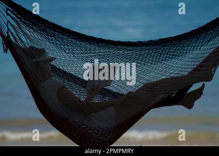 Woman reads in a hammock on a beach in Coiba National Park; Panama Stock Photo