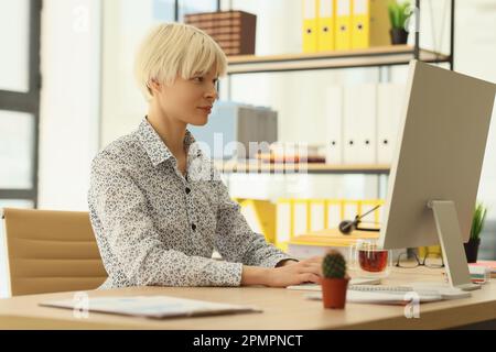 Focused woman with dyed blonde hair works on computer Stock Photo