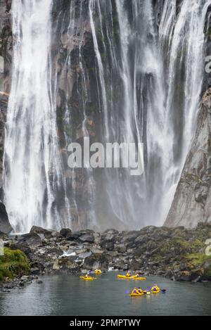 Kayakers pause at the base of Lady Bowen Falls; Milford Sound, New Zealand Stock Photo