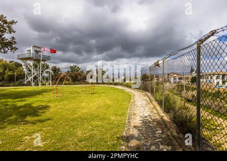 Border fence from the Turkish side with barbed wire fence, old climbing equipment and the UN watchtower in the buffer zone. Arabahmet Mahallesi, Cyprus Stock Photo