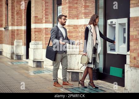 Impatient man protest in front cash machine while woman takes her money Stock Photo