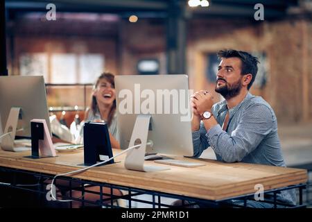 Young attractive man and woman coworkers in office sitting in front of desktops and having fun at work. Business, teamwork, students concept. Stock Photo