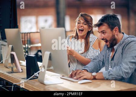 Joyful young colleagues working and looking at computer screen together, feeling joyful about good project, finding solution. Brainstorming, coffee br Stock Photo