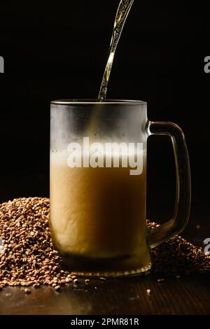 Beer is poured into a cold beer glass on a dark background. The glass is in a pile of malt. Stock Photo